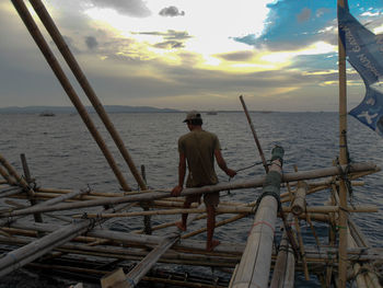 Rear view of man standing by sea against sky during sunset