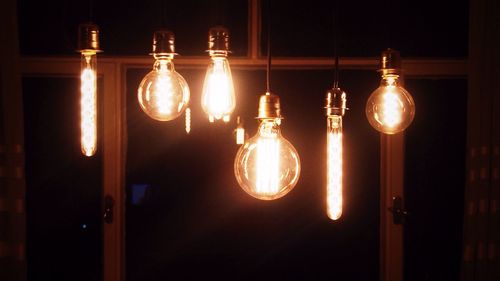 Close-up of illuminated light bulb hanging against black background