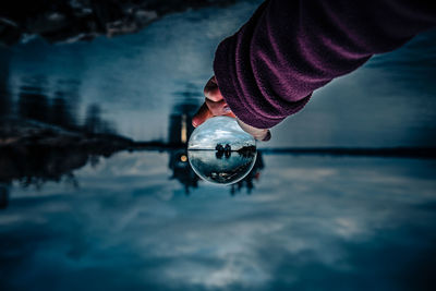 Upside down image of woman holding crystal ball against lake at night