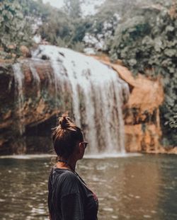 Rear view of woman standing on rock against waterfall