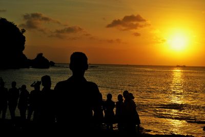 Silhouette people on beach against sky during sunset