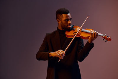 Midsection of man holding violin against black background