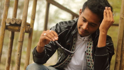 Young man holding sunglasses while sitting outdoors