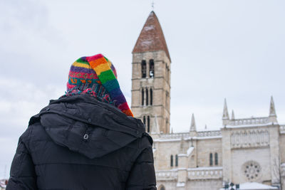 A woman in warm clothes and her back turned contemplating a medieval church in winter