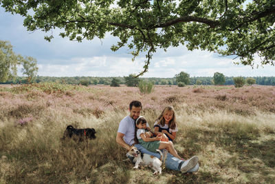 Family with father and two daughters playing with dog on field against sky