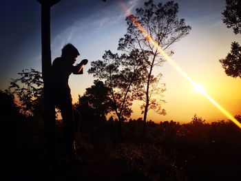 Silhouette man standing by trees against sky during sunset