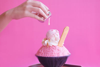 Hand holding ice cream cone against pink background