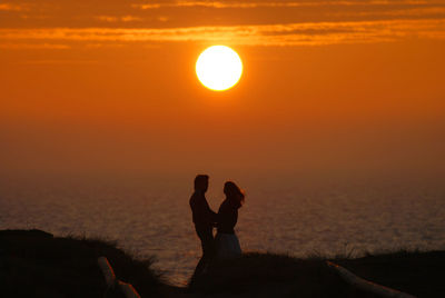 Silhouette people on sea against sky during sunset