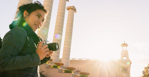 Low angle view of woman holding camera against sky