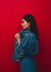 Young woman looking away against red wall