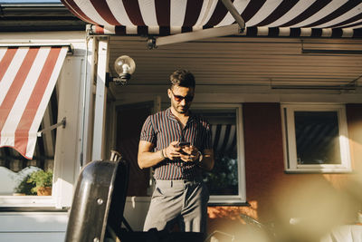 Man using smart phone while standing at back yard on sunny day