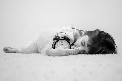 Close-up of cute girl with alarm clock lying on rug