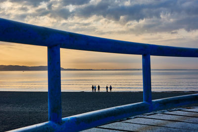 People standing on beach by sea against sky during sunrise