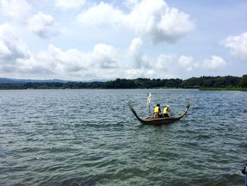 Men fishing in boat sailing on sea against sky