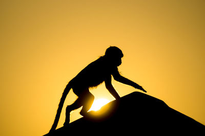 Silhouette of man sitting against orange sky