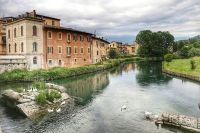 Arch bridge over river by buildings against sky