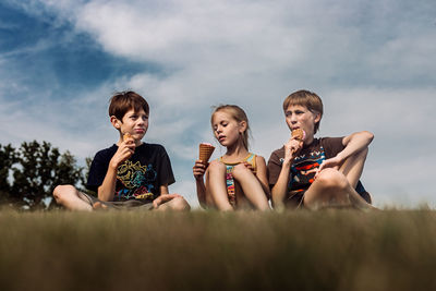 Group of friends sitting on hill eating ice cream against sky