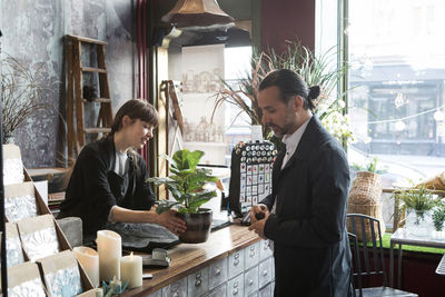 Young female owner showing potted plant to mature male customer at store