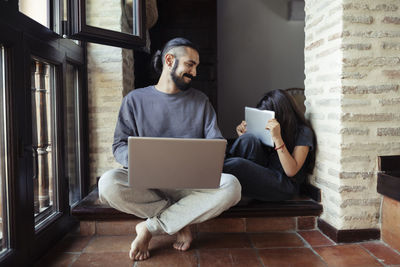 Smiling father looking at daughter hiding face with digital tablet at home