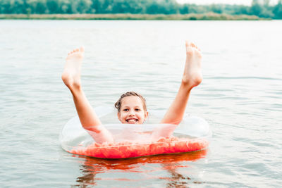 Cheerful girl sits in an inflatable ring with sticking legs in the river. local tourism. 