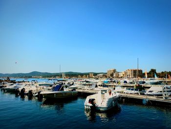 Boats moored at harbor against clear blue sky
