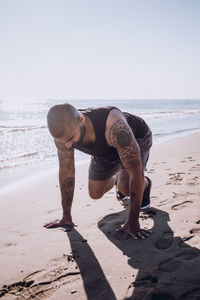 Tattooed man exercising at beach during sunny day