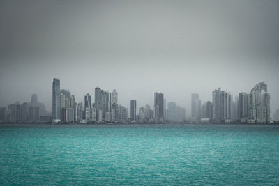 Sea by buildings against sky in city