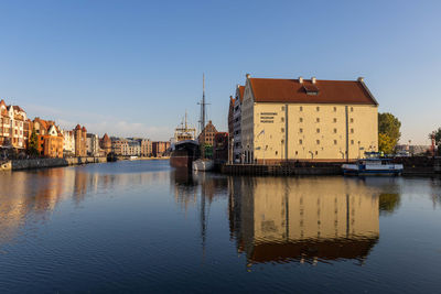 Sailboats in river by buildings against clear sky