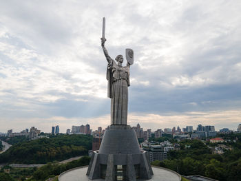 Statue in city against cloudy sky
