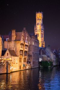 Illuminated buildings by river against sky in city at night