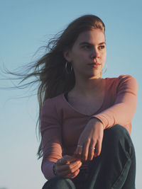 Low angle view of young woman sitting against sky