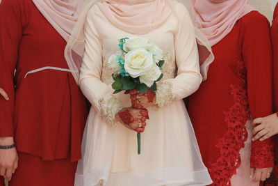 Midsection of bride holding white roses with bridesmaids