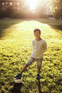 Portrait of smiling boy with soccer ball standing on grassy field at park