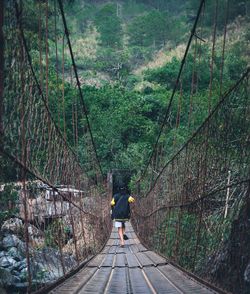 Rear view of boy running on footbridge in forest