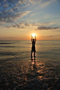 Rear view of silhouette standing on beach against sky during sunset