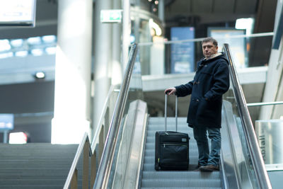 Portrait of mature man with suitcase standing on escalator at station