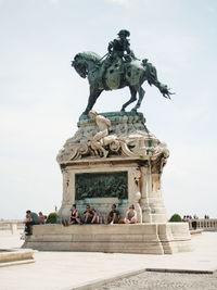 People sitting under statue against clear sky