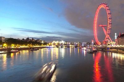 Illuminated ferris wheel by river against sky in city at night