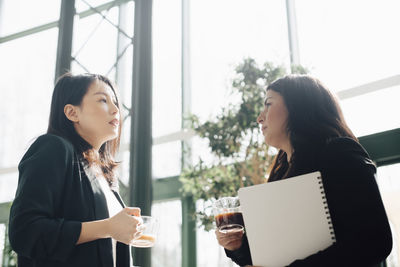 Businesswomen having coffee while discussing in brightly lit office