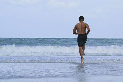 Rear view of man running on shore at beach against sky