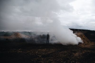 Smoke emitting from ground on field against sky with person