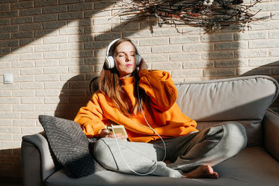 Young woman sitting on sofa against wall