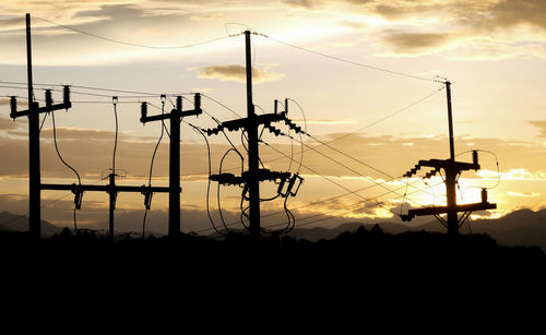 Silhouette electricity pylon against dramatic sky during sunset