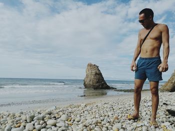 Young man standing on rock at beach against sky