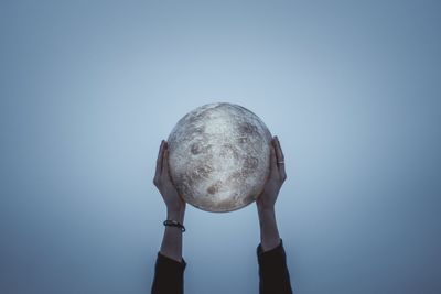 Cropped hands of person holding ball against sky