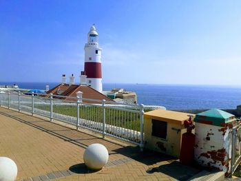 Lighthouse by sea against clear blue sky