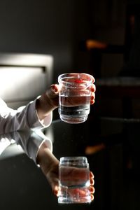 Close-up of hand holding water in glass with reflection on table