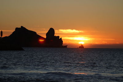 Silhouette rocks in sea against sky during sunset