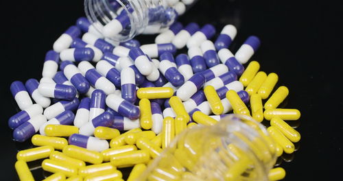 Close-up of pills spilling from bottle against black background