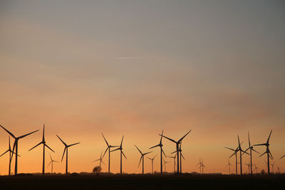 Silhouette wind turbines on land against sky during sunset